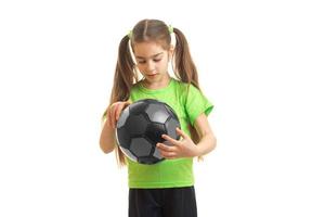 kleines Mädchen in grüner Sportuniform mit Fußball in den Händen foto
