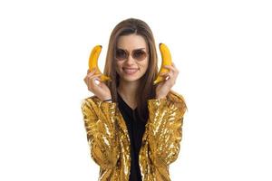 Fröhliche, stilvolle Frau in goldener Jacke mit Bananen foto