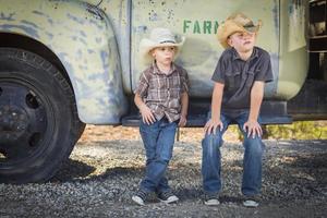 zwei Jungen mit Cowboyhüten, die sich an einen antiken Lastwagen lehnen foto