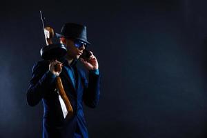 Zurückhaltendes Porträt eines jungen Gangsters mit Hut in der Dunkelheit foto