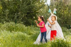 zwei glückliche kleine kinder sitzen auf dem gras und lesen märchen in der nähe eines zeltes in ihrem hof. home camping urlaubskonzept foto