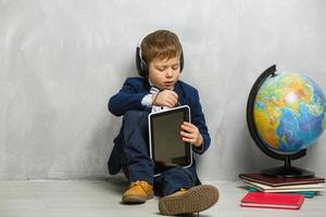 Fröhlicher kleiner Junge, der ein digitales Tablet mit leerem Bildschirm im Klassenzimmer hält und lächelt foto