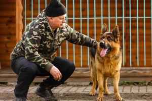 der mann beeinflusst den hund, gehorsamer und liebevoller hund, gefangene hunde ziehen ihre köpfe durch die gitter, der junge mann füttert einen hund, der mann trainiert foto