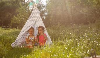 zwei glückliche kleine kinder sitzen auf dem gras und lesen märchen in der nähe eines zeltes in ihrem hof. home camping urlaubskonzept foto