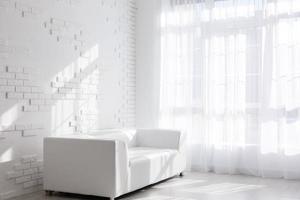 Helles, minimalistisches Wohnzimmerinterieur mit weißem Sofa am Fenster und schwarzem Hocker foto