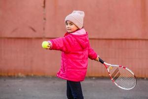 kleines süßes mädchen, das draußen tennis spielt foto