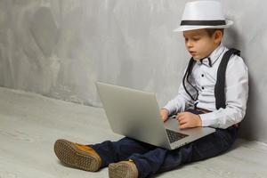 kleiner Junge mit Laptop vor grauem Wandhintergrund foto