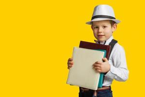 glücklicher lächelnder junge mit brille und daumen nach oben geht zum ersten mal zur schule. Kind mit Schultasche und Buch. Kind drinnen des Klassenzimmers mit Tafel auf einem Hintergrund. zurück zur Schule. foto