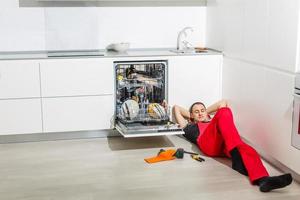 junger Handwerker, der in der Küche ein Spülrohr repariert foto