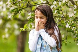 Kleines Mädchen putzt sich die Nase in der Nähe des blühenden Frühlingsbaums foto