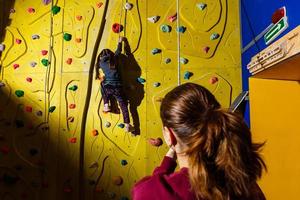 Lehrer hilft Mädchen beim Klettern an der Wand im Fitnessstudio foto
