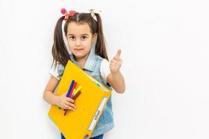 glückliches süßes kleines schulmädchen, das schultaschenrucksack und bücher trägt, die in der bildung und zurück zum schulkonzept lokalisiert auf weißem hintergrund lächeln foto