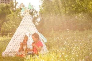 Zwei glückliche lachende kleine Mädchen im Campingzelt auf dem Löwenzahnfeld foto