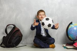 kleiner Schüler mit einem Ball auf grauem Hintergrund foto
