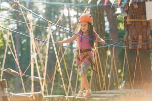 entzückendes kleines mädchen, das ihre zeit im kletterabenteuerpark an warmen und sonnigen sommertagen genießt. Sommeraktivitäten für kleine Kinder. kind hat spaß in den schulferien. foto