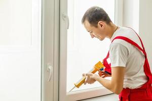 Bauarbeiter, der das Fenster im Haus mit Schaumklebeband versiegelt foto