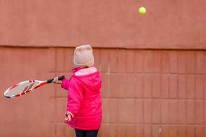 kleines süßes mädchen, das draußen tennis spielt foto