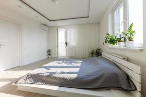 graue Decke auf dem Bett mit hölzernem Kopfteil in einem einfachen Schlafzimmer mit dunklem Poster und Stuhl unter dem Fenster foto