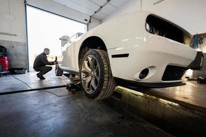 mechaniker in der reparaturstation, die mit muskelautos arbeitet. inspiziert den laufenden Teil des Rades. foto