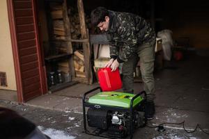 Mann trägt Militärjacke, gießt Benzin aus Kanister in tragbaren mobilen Backup-Standby-Generator. foto