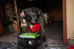Mann trägt Militärjacke, gießt Benzin aus Kanister in tragbaren mobilen Backup-Standby-Generator. foto