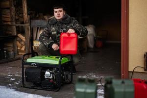 Mann trägt Militärjacke, gießt Benzin aus Kanister in tragbaren mobilen Backup-Standby-Generator. foto