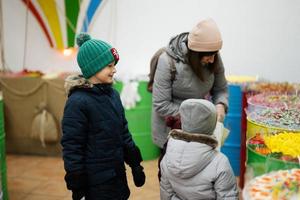 Glückliche kleine Kinder mit Mutter in einem Süßwarenladen wählen Süßigkeiten, Marmeladenbonbons und legen sie in eine Papiertüte. foto