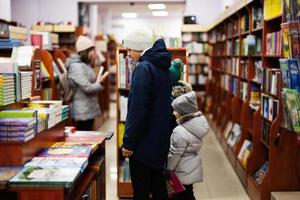 Kinder in Jacke erreichen ein Buch aus dem Bücherregal in der Bibliothek. Lernen und Bildung europäischer Kinder. foto