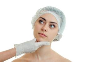 Der Chirurg im Handschuh überprüft das Gesicht eines schönen Mädchens in einer speziellen Kappe für die Haarnahaufnahme foto