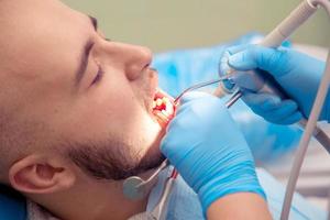 Porträt eines jungen erwachsenen männlichen Patienten nimmt eine zahnärztliche Behandlung in der Zahnarztpraxis vor foto