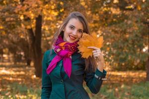 Mädchen steht im Herbstpark und hält die Blätter in der Hand foto