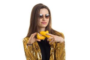 Porträt einer erstaunlichen Brünetten mit Brille und einer goldenen Jacke, die Bananen in den Händen hält foto