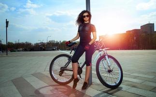 Glamour trägt Frau mit Sonnenbrille auf dem Fahrrad zur Schau foto