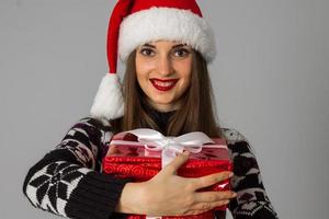 frau im warmen pullover und in der weihnachtsmütze mit rotem geschenk foto