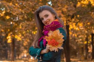 Fröhliches junges Mädchen im Herbstpark hält einen Strauß Blätter in der Hand und lächelt foto