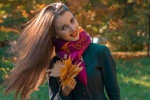 attraktives junges mädchen mit langen haaren in einem rosa schal hält seine blätter in der hand und lächelt foto