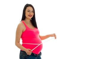 junge schwangere Frau posiert mit Maßband auf ihrem Bauch isoliert auf weißem Hintergrund foto