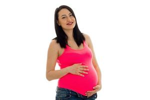 glückliche schwangere zukünftige mutter im rosa hemd, das lokalisiert auf weißem hintergrund aufwirft foto