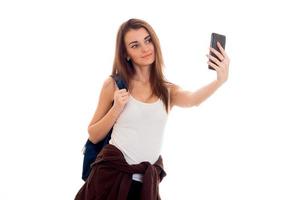 Fröhliche junge Studentin mit Rucksack macht Selfie auf ihrem Handy isoliert auf weißem Hintergrund. Konzept der Studentenjahre. Studienkonzept. foto