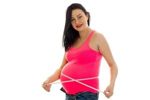 Glückliche schwangere zukünftige Mutter im rosafarbenen Hemd misst ihren Bauch isoliert auf weißem Hintergrund foto