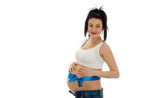 süßes junges brünettes schwangeres Mädchen mit blauem Klebeband auf ihrem Bauch posiert isoliert auf weißem Hintergrund foto
