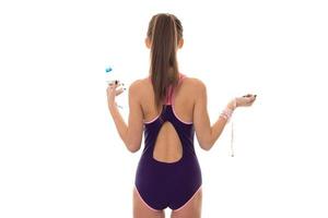 schlankes junges brünettes Mädchen im Badeanzug mit Maß und Flasche Wasser in den Händen von der Rückseite isoliert auf weißem Hintergrund foto