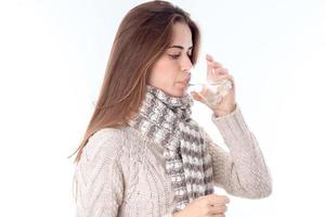 Mädchen in einem warmen Pullover steht seitlich und trinkt ein Glas Wasser isoliert auf weißem Hintergrund foto