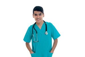 Porträt eines jungen, fröhlichen, brünetten Mannes Arzt in blauer Uniform mit Stethoskop, der vor der Kamera lächelt, isoliert auf weißem Hintergrund foto