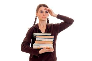 Müdes, intelligentes Studentenmädchen in brauner Sportkleidung mit vielen Büchern in ihren Händen, die isoliert auf weißem Hintergrund posieren foto