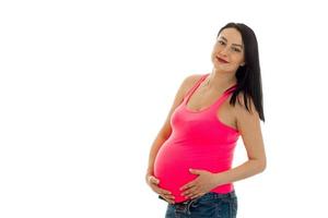 Porträt einer jungen süßen schwangeren Frau, die ihren Bauch berührt und vor der Kamera posiert, isoliert auf weißem Hintergrund foto