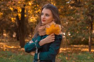 Nachdenkliches Mädchen steht auf der Straße und hält Herbstblätter in der Hand foto