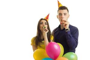 junger Mann mit Mädchen feiert Geburtstag und hält viele Luftballons und Hörner in der Nähe des Mundes foto