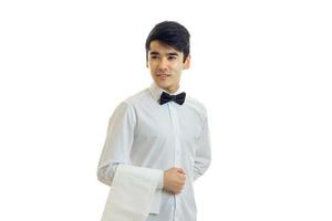 Der charmante junge Kellner in einem weißen Hemd sieht in die Ferne und hält ein Handtuch bereit foto