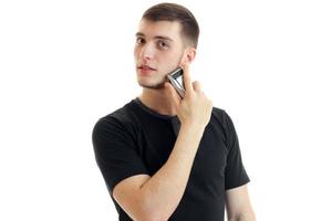 Attraktiver junger Mann im schwarzen T-Shirt schaut weg und rasiert einen Bartschneider aus nächster Nähe foto